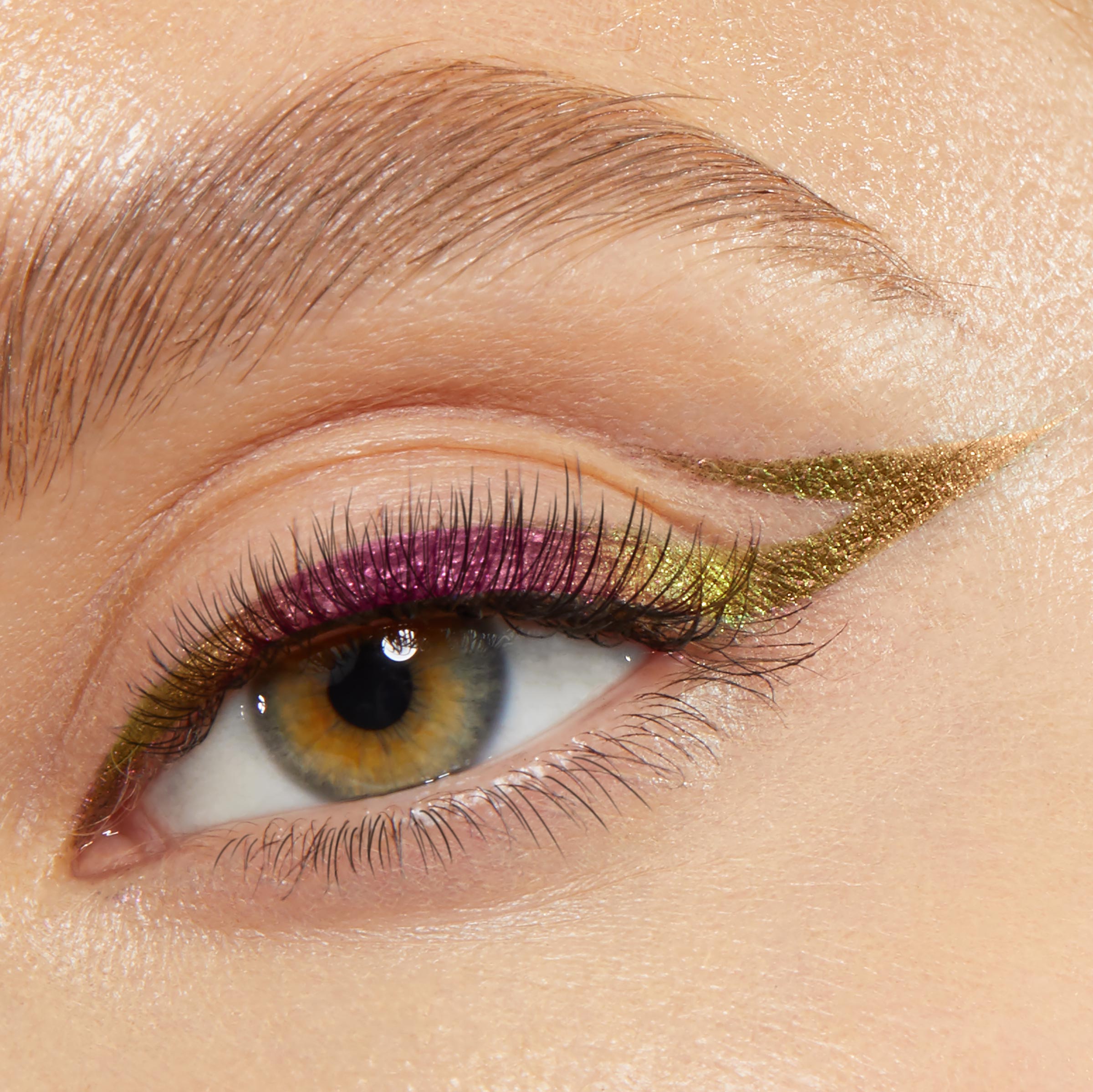 Chrome winged eyeliner creates a sharp elongated flick across a close-up eye, shifting olive-gold with magenta-lime along the lash line, showcasing ColourPop Chrome Crème Gel Liner, shade Chrome Hearted, on natural lashes and a groomed brow.