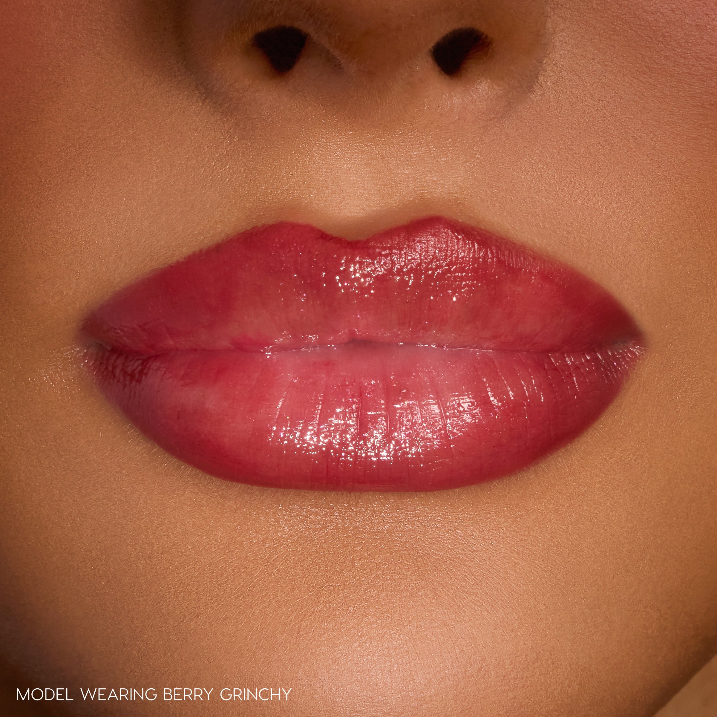 Glossy, berry-pink lips wearing ColourPop So Juicy Plumping Gloss Stick in Berry Grinchy, catching light to show a full, hydrated shine in a close-up studio shot of the lower face.