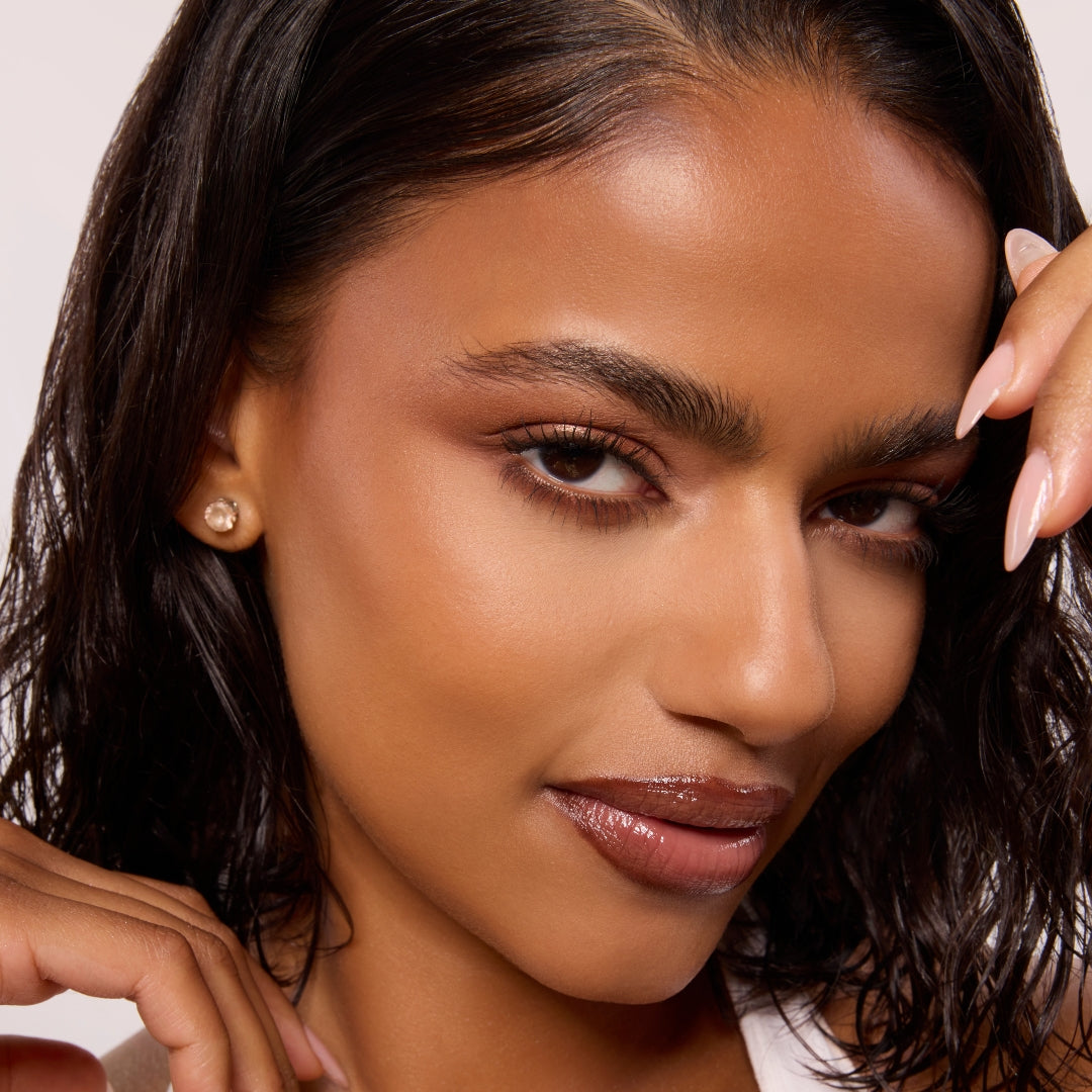 Warm bronze eye look wearing Feelin Wild Shadow Palette Set, a ColourPop Shadow Palette Set, blending matte terracotta and soft shimmer on lids, shown close-up with glossy nude lips, pearl stud earrings, and manicured nude nails on a light background.