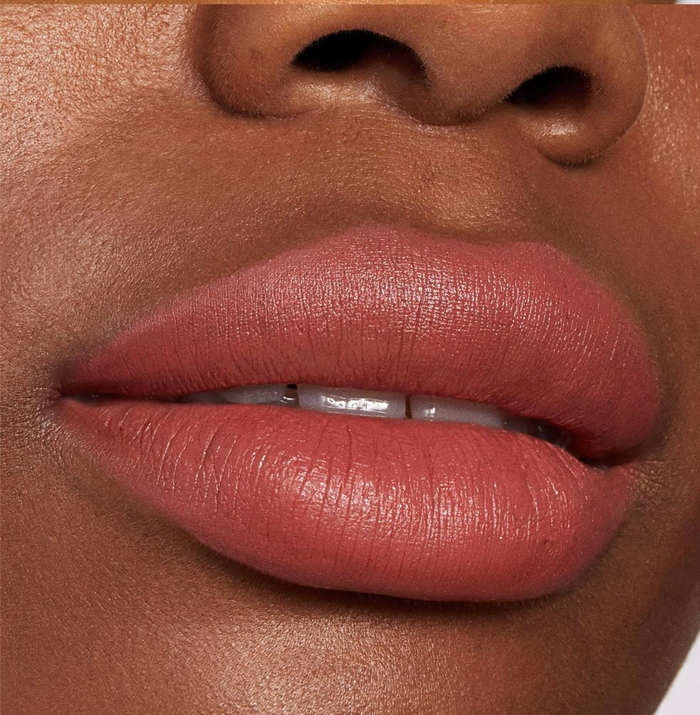 Lips wearing ColourPop Lippie Stix Brink, a warm rosy terracotta nude in a soft‑matte finish, shown in a close-up to highlight smooth, even coverage and creamy texture.
