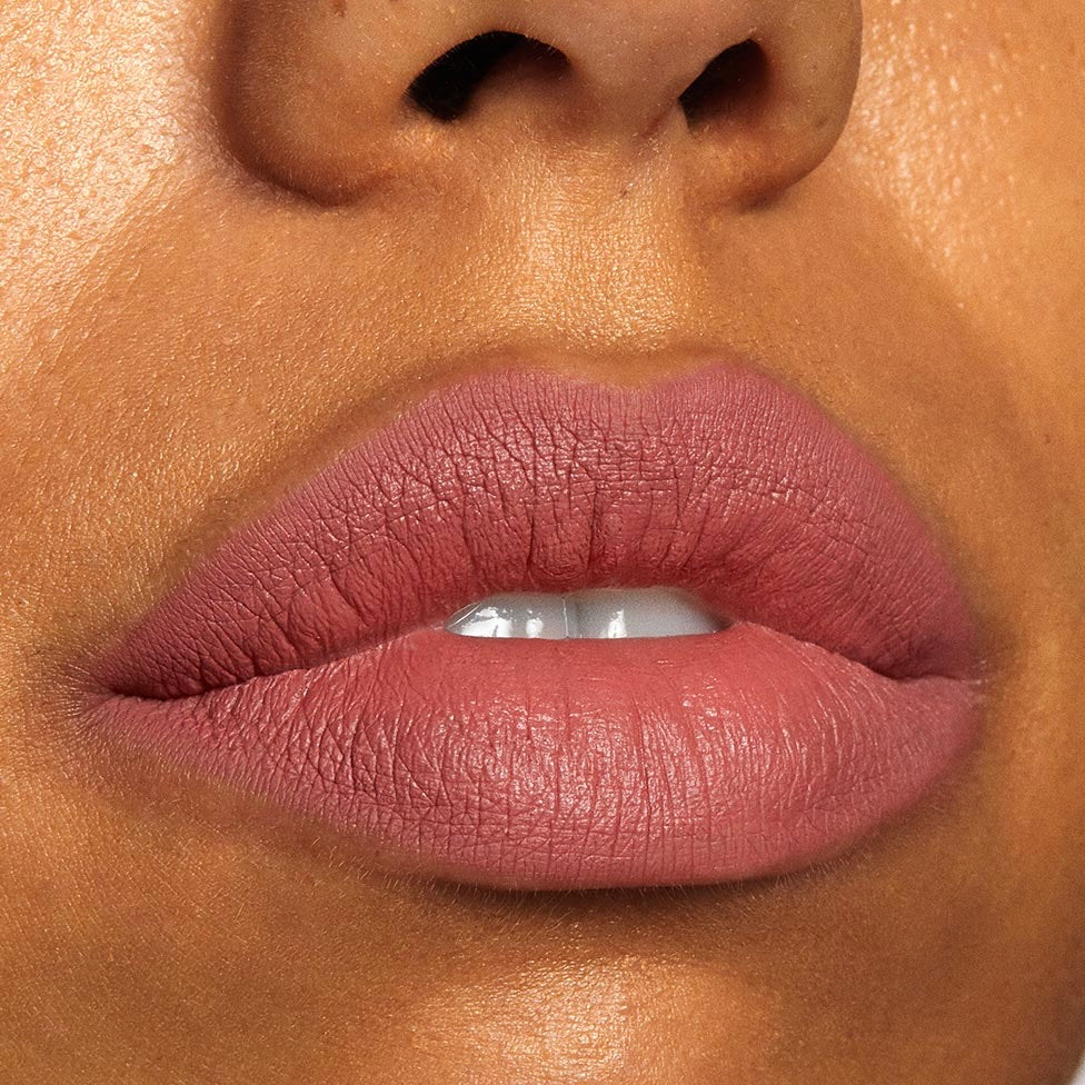 Lips wearing Brink Lippie Stix, a warm rosy‑mauve nude, show full‑coverage soft‑matte payoff in a close‑up beauty swatch of ColourPop Lippie Stix on smooth skin.