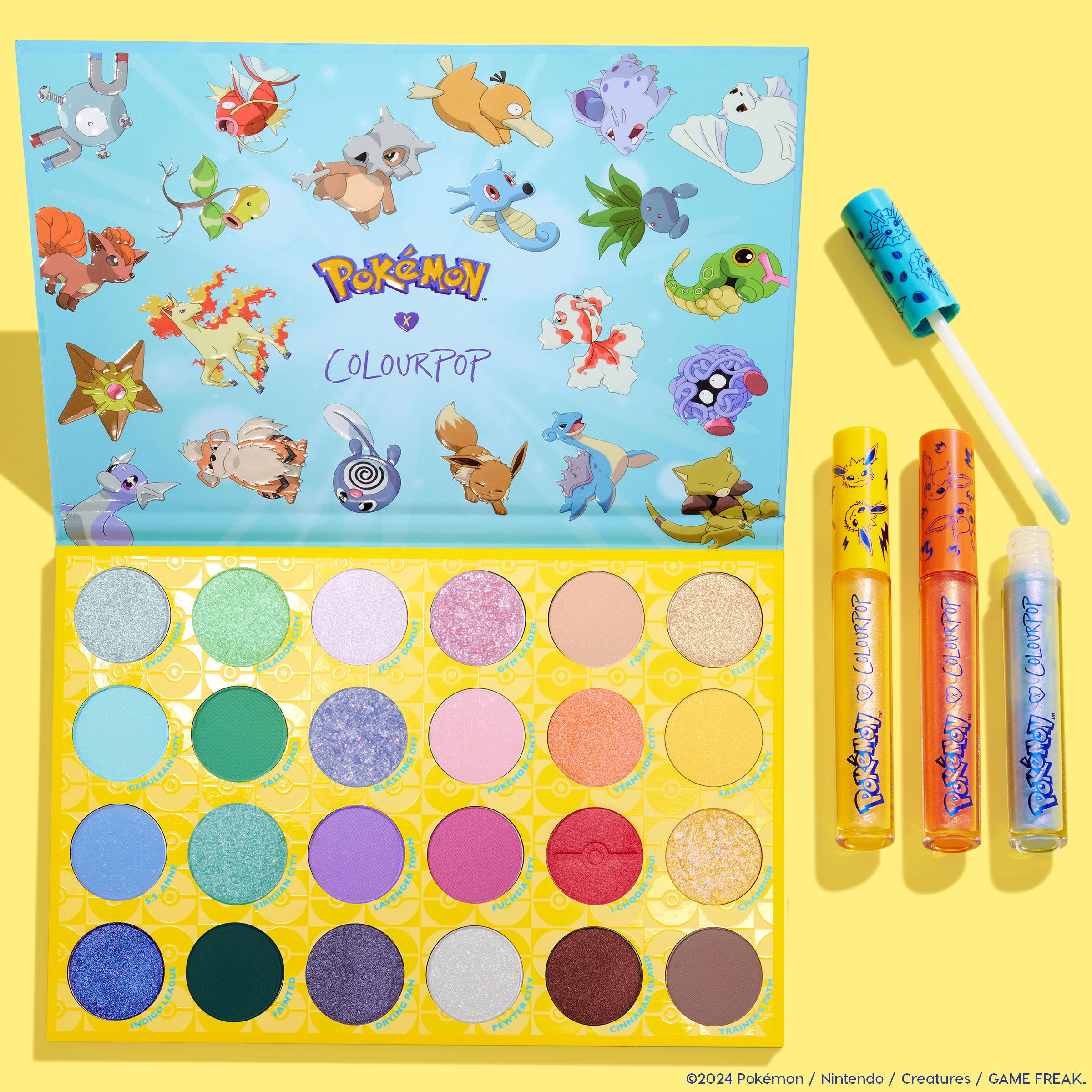 Ready For Battle ColourPop Shadow Palette & Ultra Glossy Lip Set showcasing an open 30-pan eyeshadow palette with Pokémon artwork and three glosses (yellow, orange, blue, one wand open) arranged in a bright yellow flatlay background.