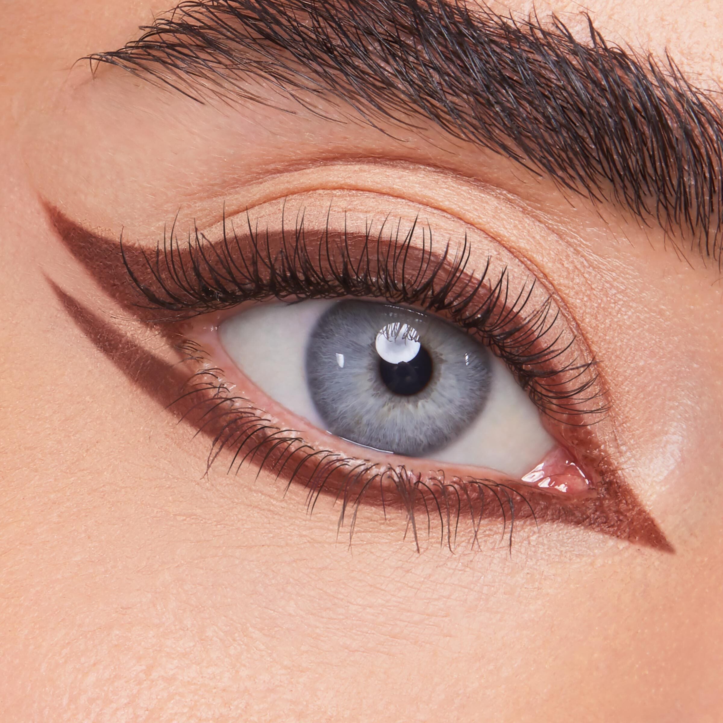 ColourPop Crème Gel Liner Sunnyvale tracing a sharp rich-brown double wing on a blue eye - lining upper and lower lashes with a pointed inner corner - over nude shadow, showcasing precise, long-wear crème gel eyeliner for graphic looks.