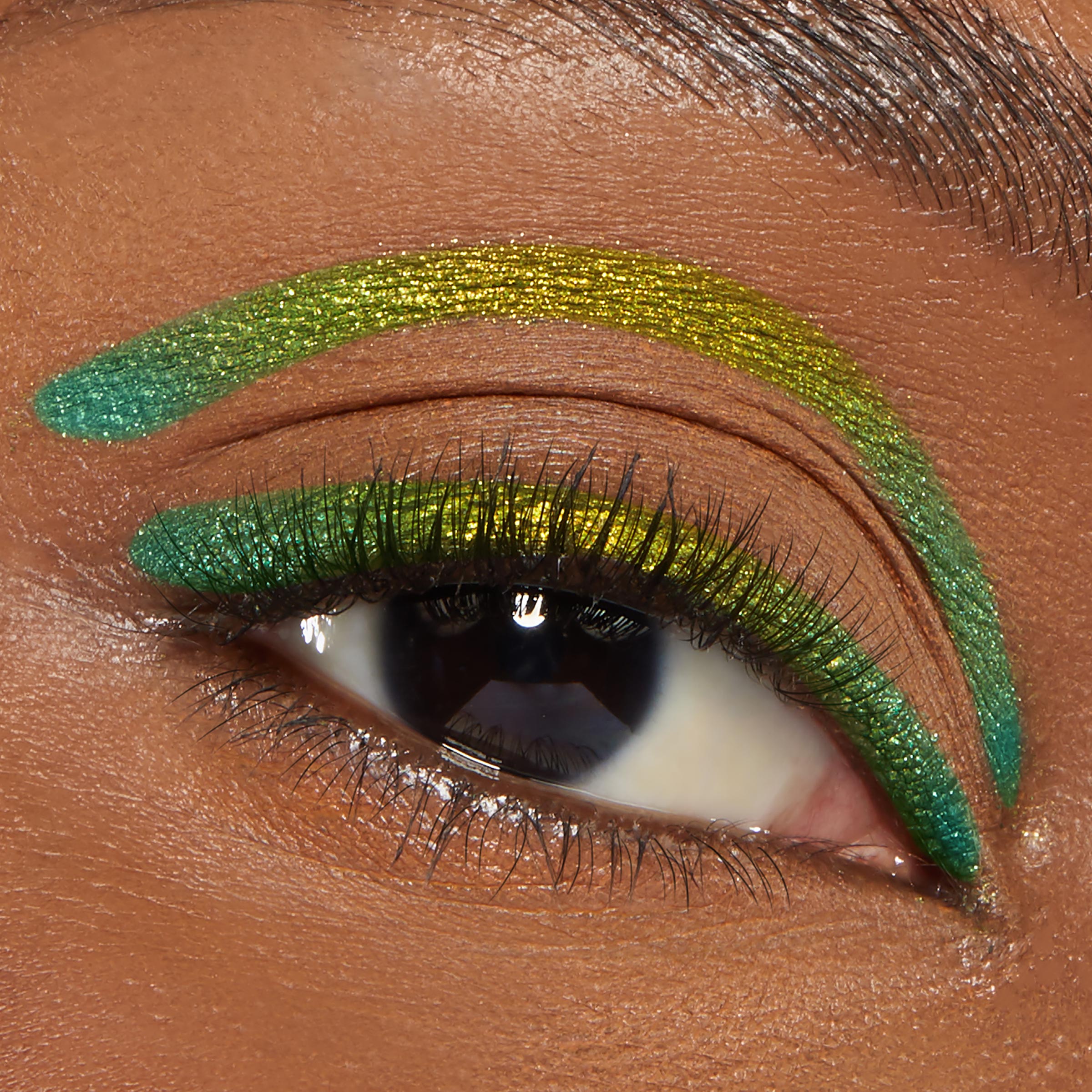 Macro eye wears ColourPop Chrome Crème Gel Liner in Chrome Hearted, a metallic green-to-gold shift, lining the upper lash line and a bold arc above the crease on warm brown skin, showcasing smooth, opaque payoff.