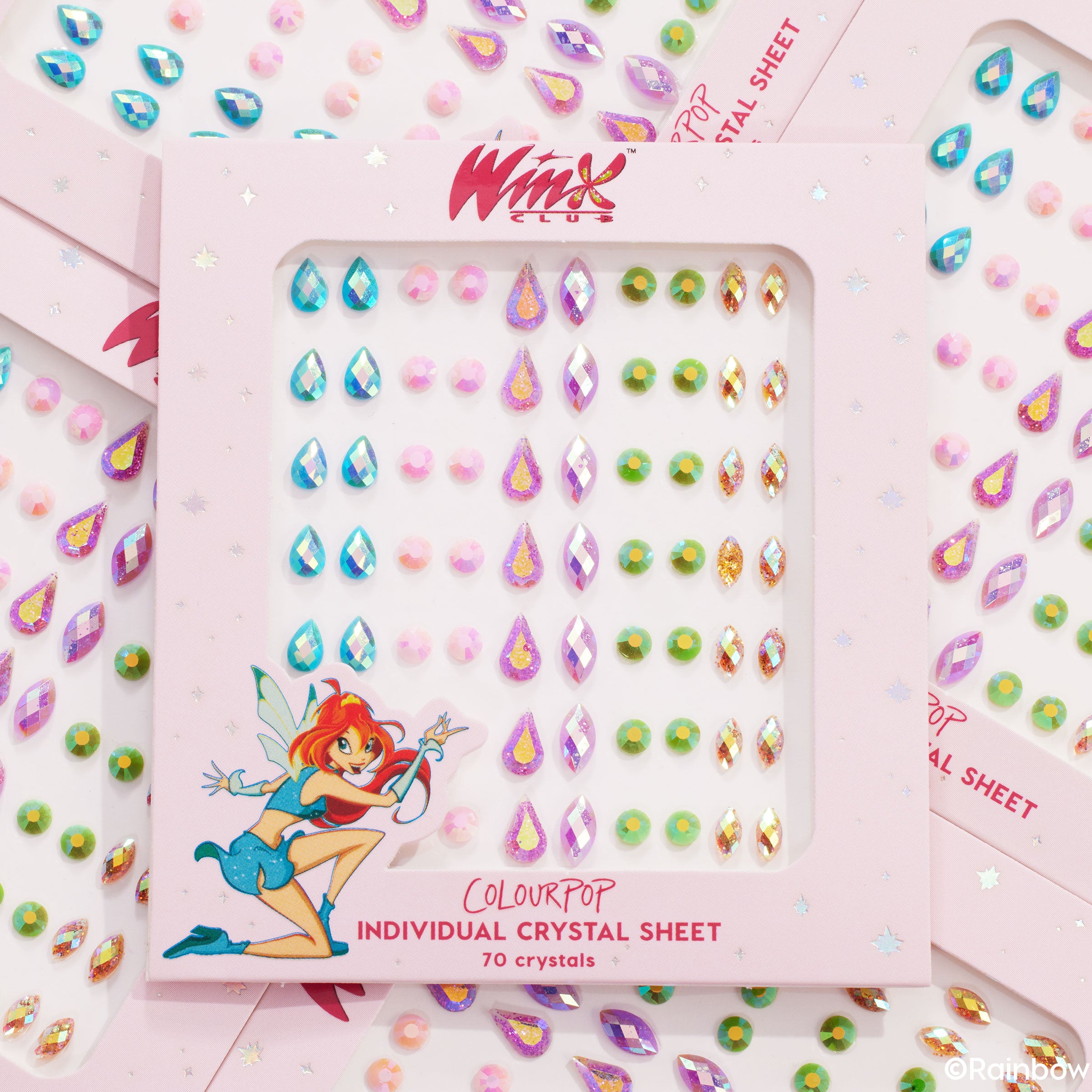 ColourPop Crystal Face Jewels Individual sheet sparkles in a pink Winx Club box, showing 70 self-adhesive gems in teardrop, round, and diamond shapes - iridescent blues, pinks, greens, and gold - flatlay of overlapping packs for festival makeup.