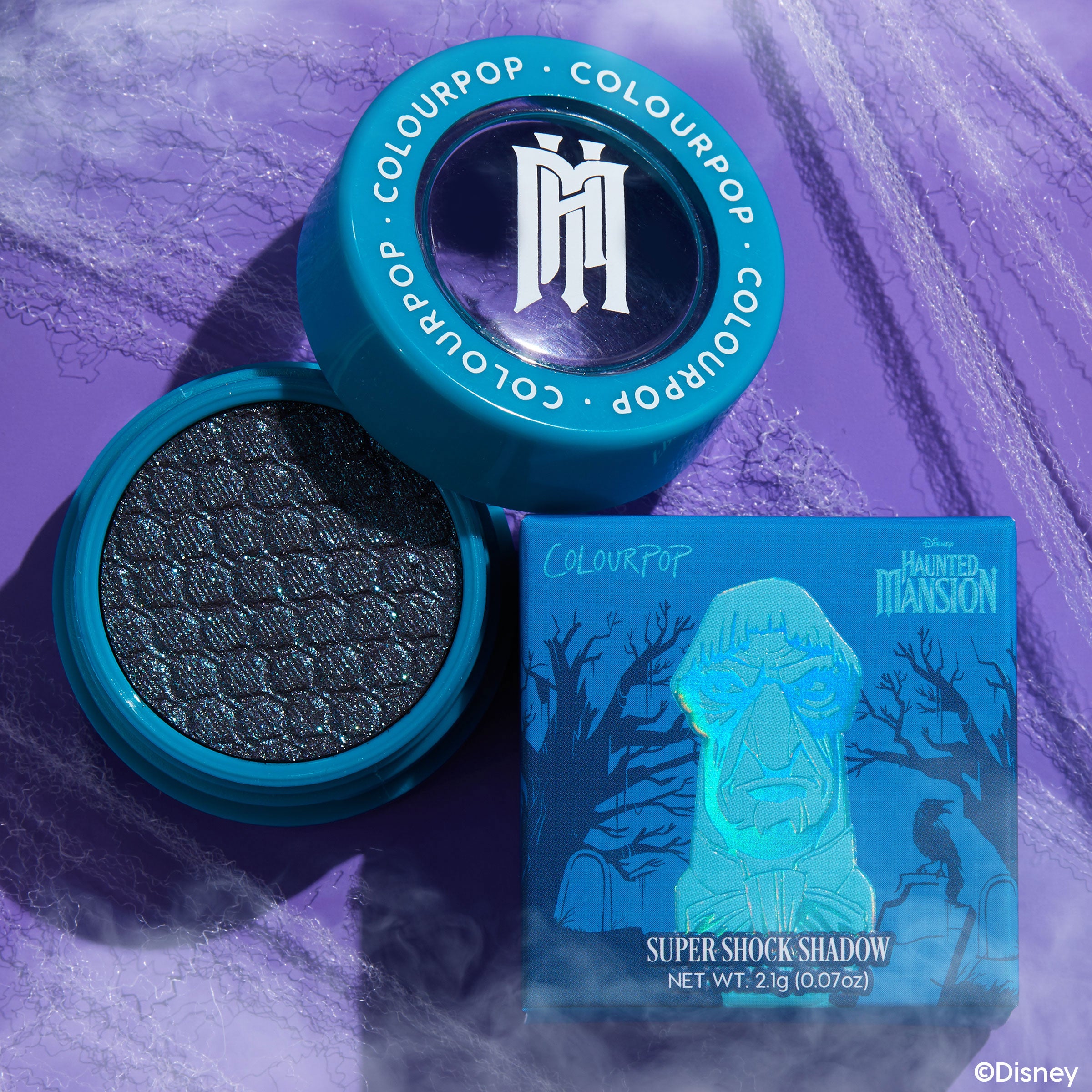 Frightful ColourPop Super Shock Shadow opens to reveal a charcoal-black cream shadow packed with teal sparkle, housed in a teal pot beside Disney Haunted Mansion box art, styled on a purple, cobwebbed background.