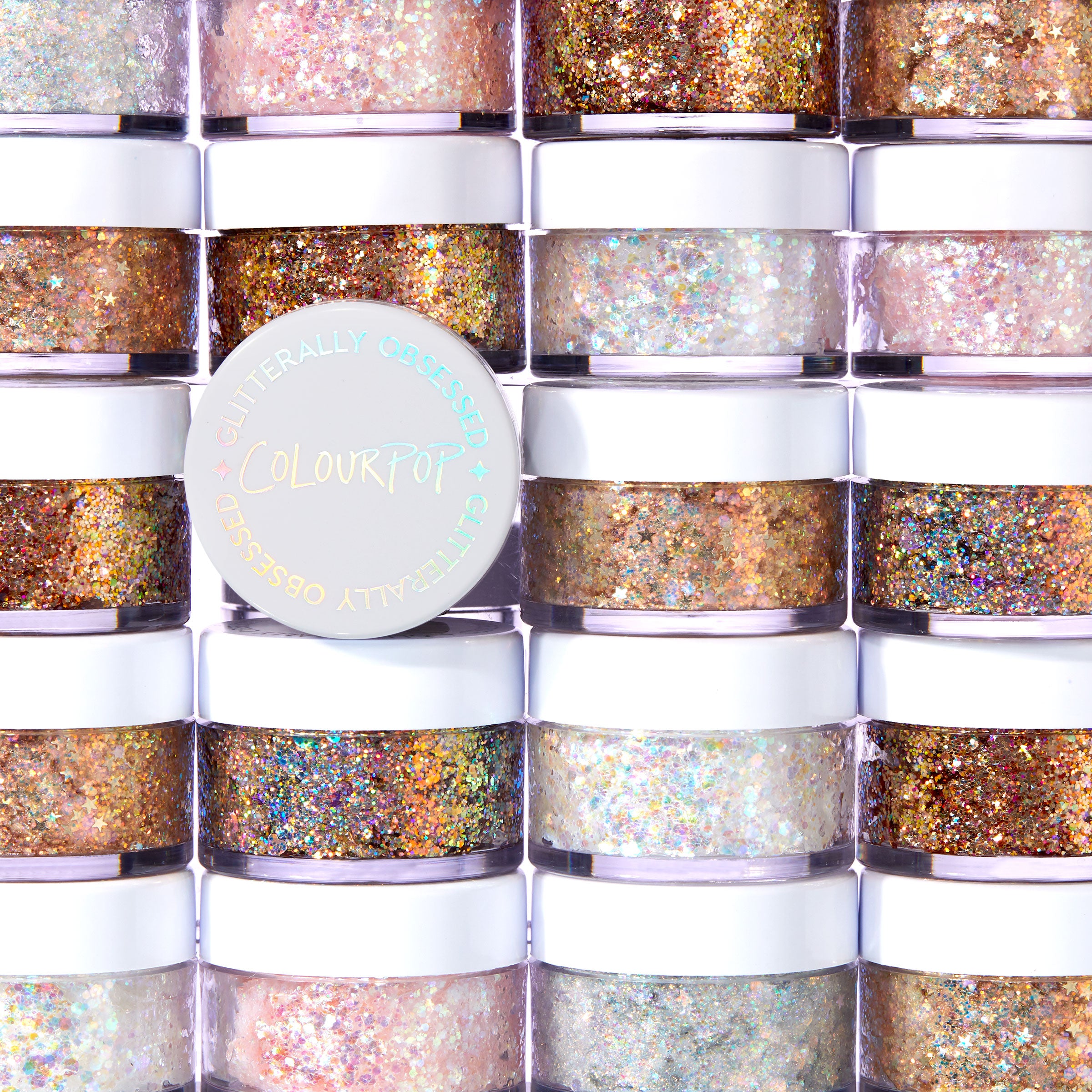 Ur A Firework ColourPop Glitter Gel jar shining with holographic sparkle, resting on stacked white-lidded pots, showcasing the Glitterally Obsessed collection in a bright studio setting with multicolor glitter visible through clear sides.
