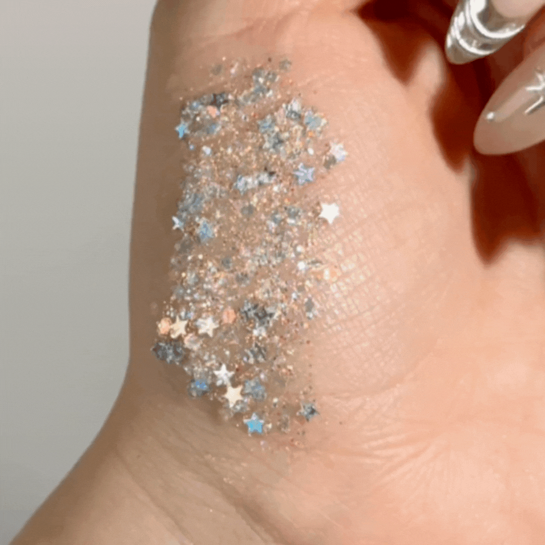 Ur A Firework ColourPop Glitter Gel swatched on the back of a hand, sparkling with chunky star and hex glitter in silver, blue, and iridescent hues suspended in clear gel, shown close-up to highlight texture and payoff.