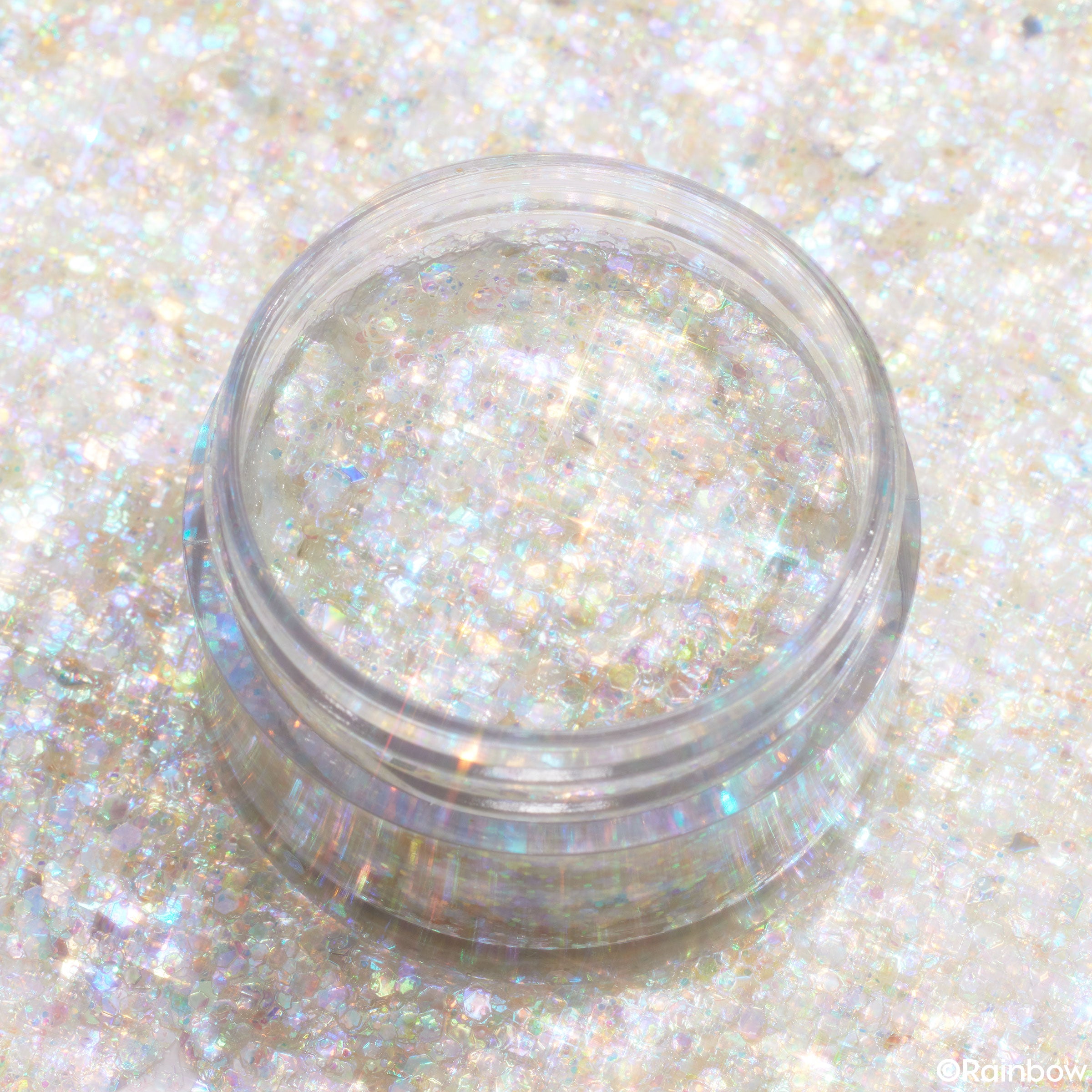 ColourPop Glitter Gel Enchantix shimmering in a clear plastic pot, chunky iridescent rainbow sparkles suspended in translucent gel and catching light, product jar styled in flatlay on a matching opalescent glitter background.