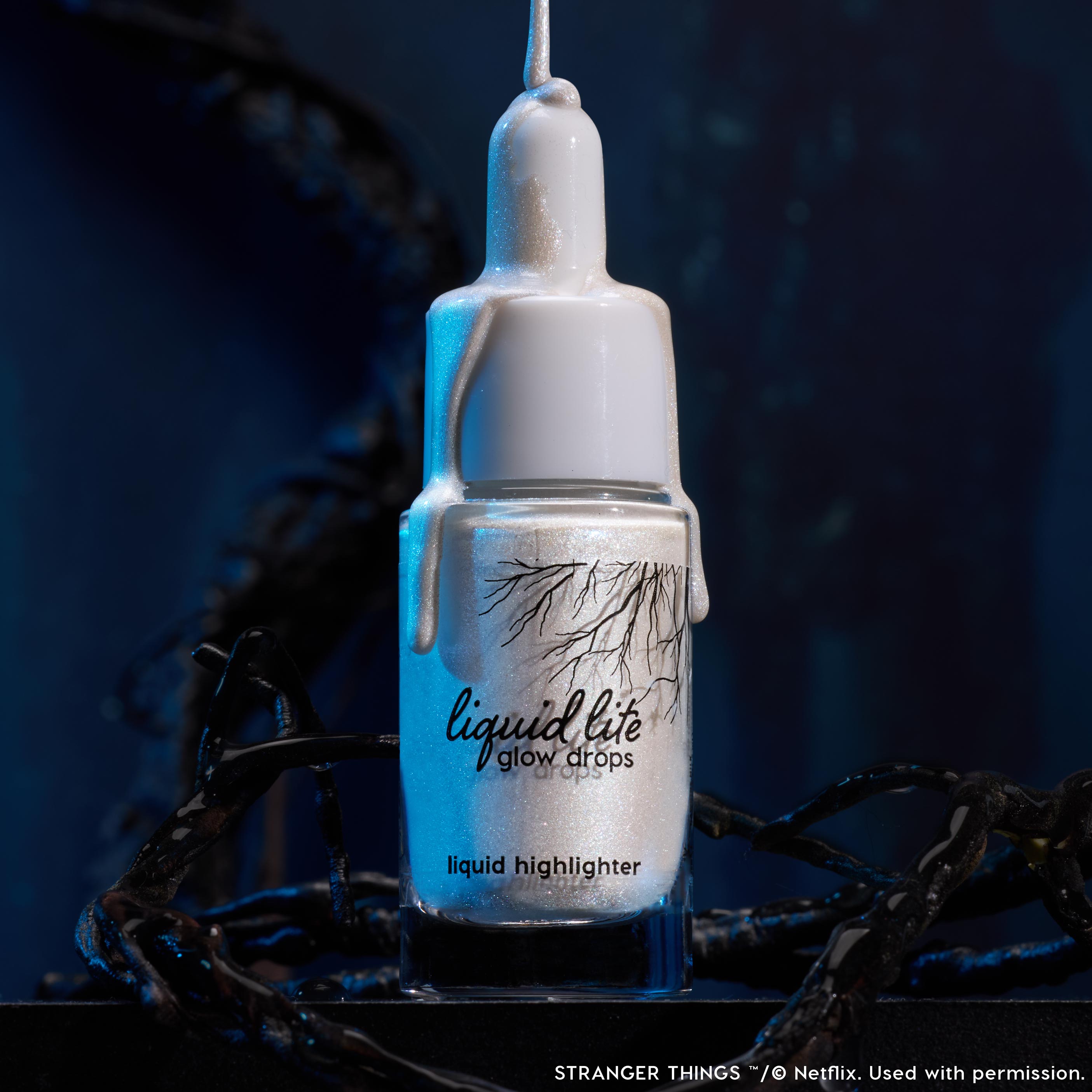 Hawkins Milk ColourPop Liquid Highlighter gleams in a clear dropper bottle as milky pearlescent drips cascade over the cap, staged among dark vine-like tendrils and moody blue light for an Upside Down–inspired, sci‑fi glow.