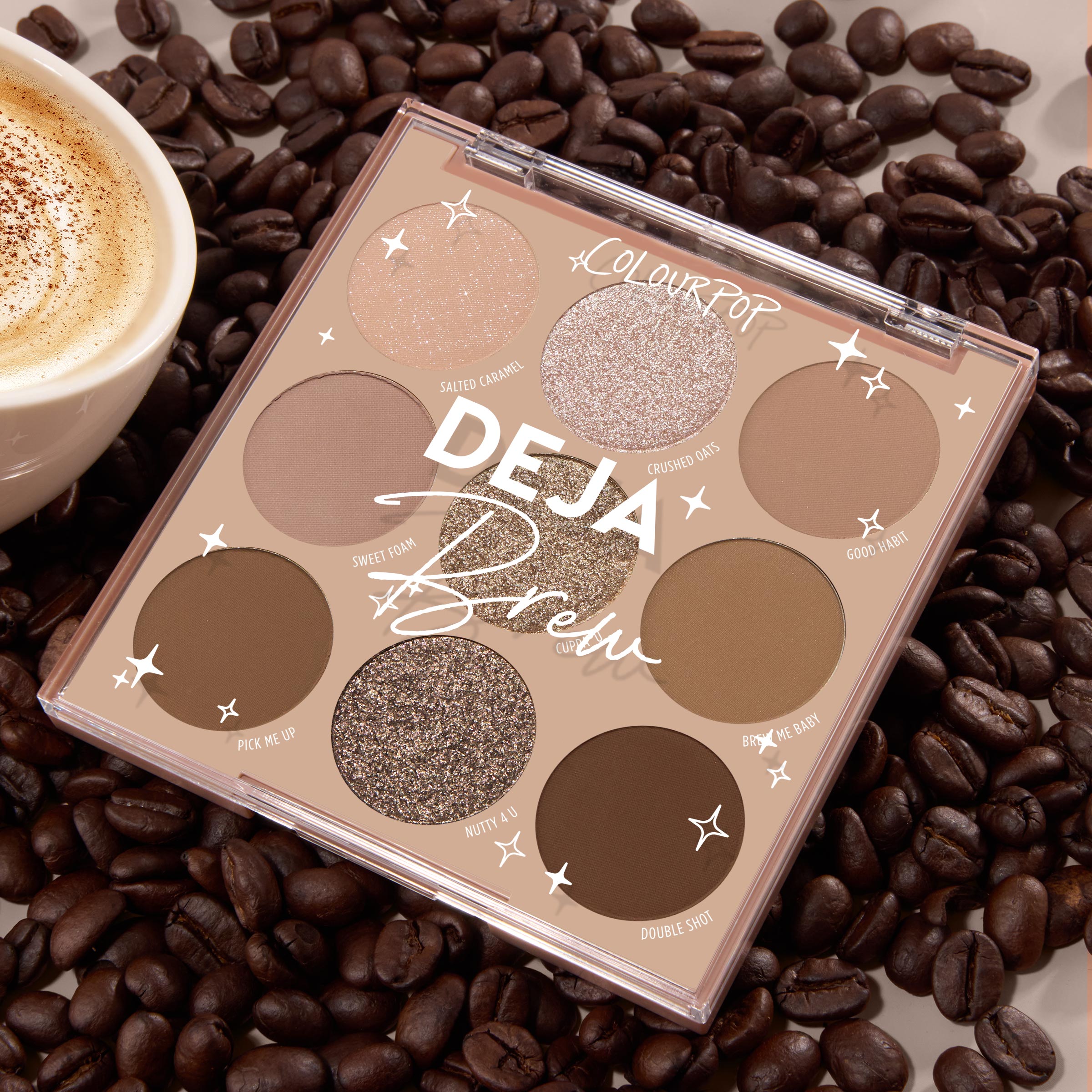 Deja Brew ColourPop Shadow Palette displaying nine coffee-inspired shades - matte and shimmer browns, taupes, and champagne - opened in a 3x3 layout on roasted coffee beans next to a latte, highlighting neutral eye looks.