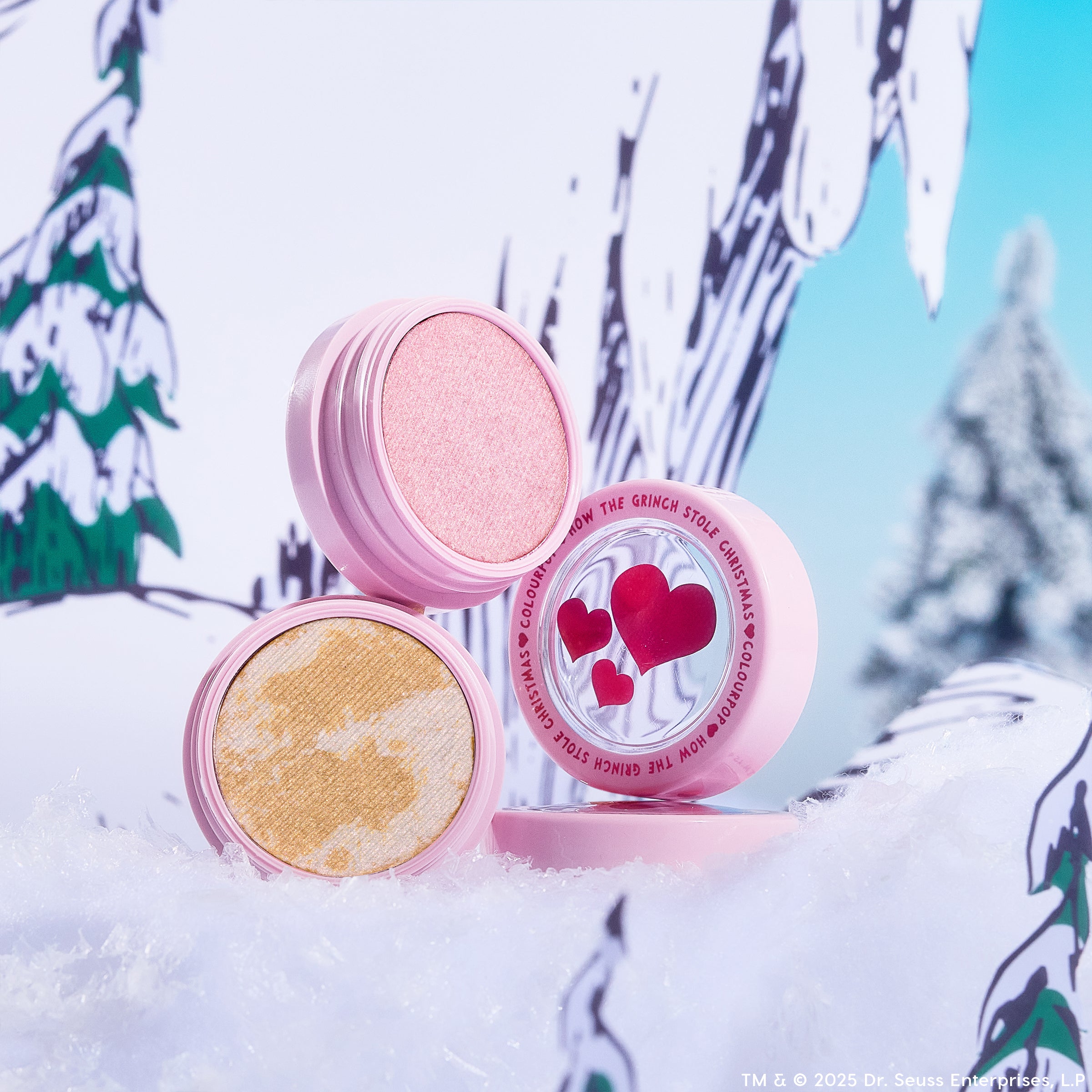ColourPop Change of Heart Super Shock Highlighter Kit, two pink compacts opened to show a soft pink shimmer and marbled gold highlighter, heart-detailed lids propped in a snowy, whimsical Dr. Seuss–style forest backdrop.