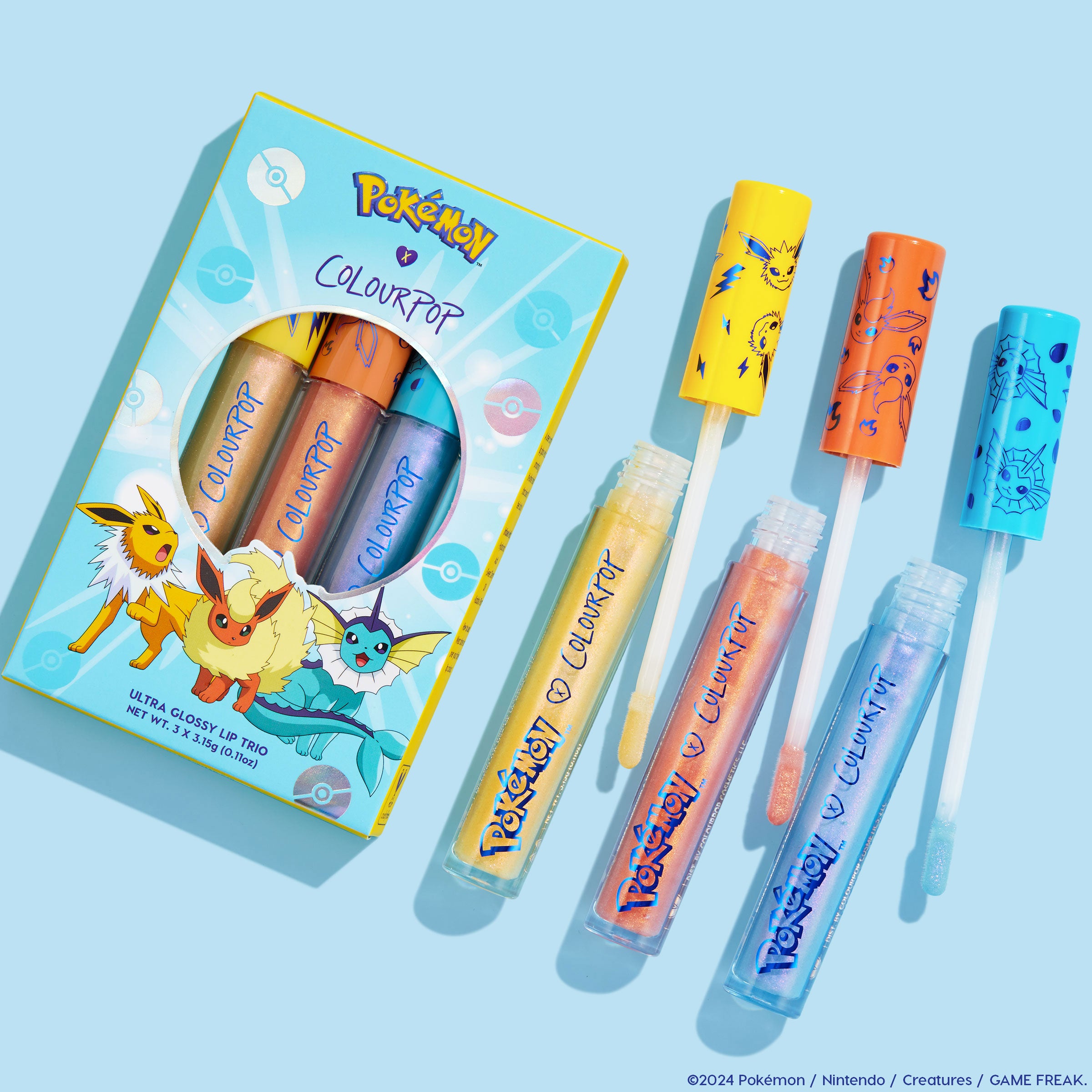 Ready For Battle shadow palette & ultra glossy lip set from the Pokémon x ColourPop Collection shown flatlay on a blue background, with three ColourPop lip gloss tubes pulled out to reveal wands and colorful Pokémon-themed caps.