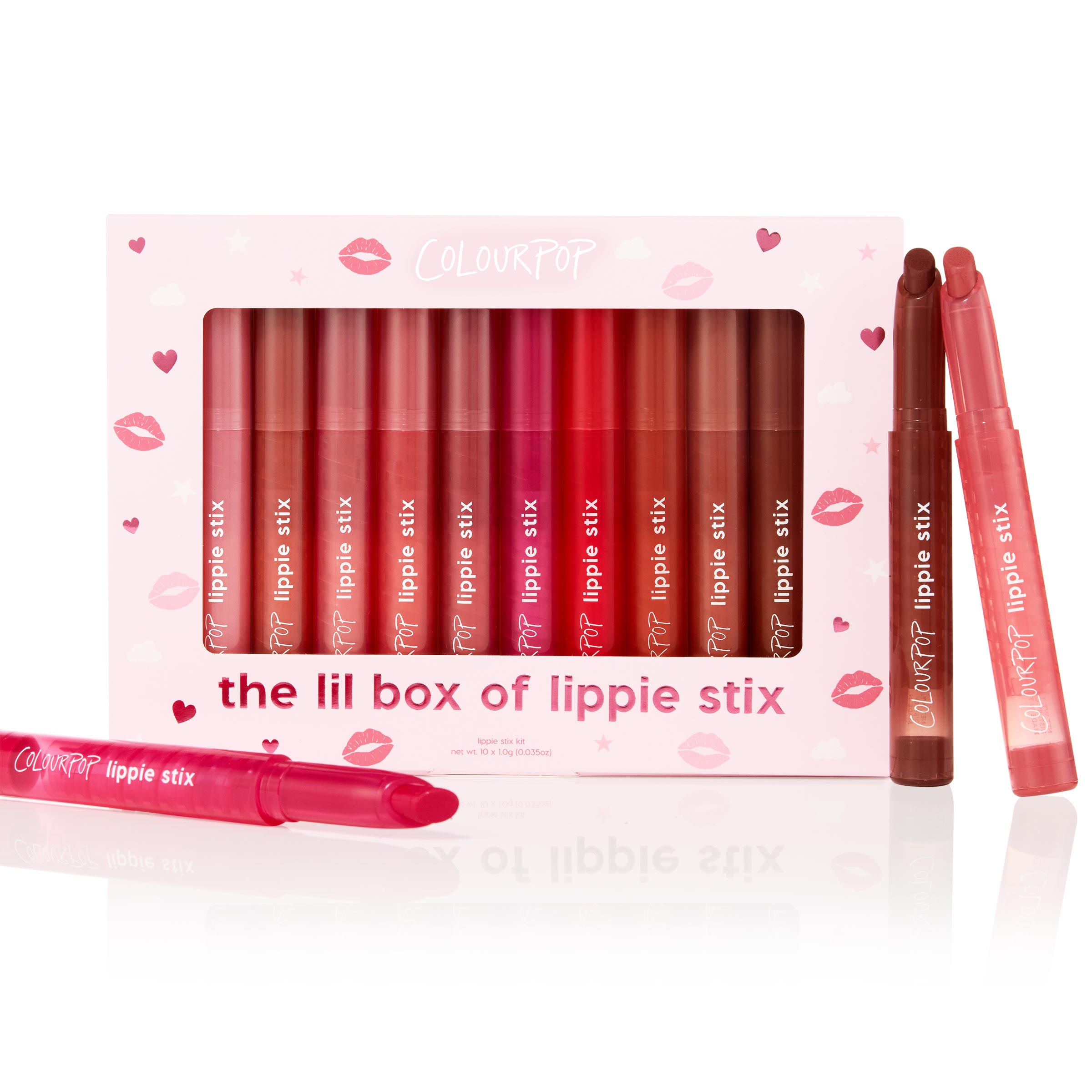 ColourPop Lippie Stix arranged in The Lil Box of Lippie Stix, a 10-shade set in a pink heart-and-kiss box, showing a gradient from nude to bold reds with two uncapped tubes in front, studio-lit on white.
