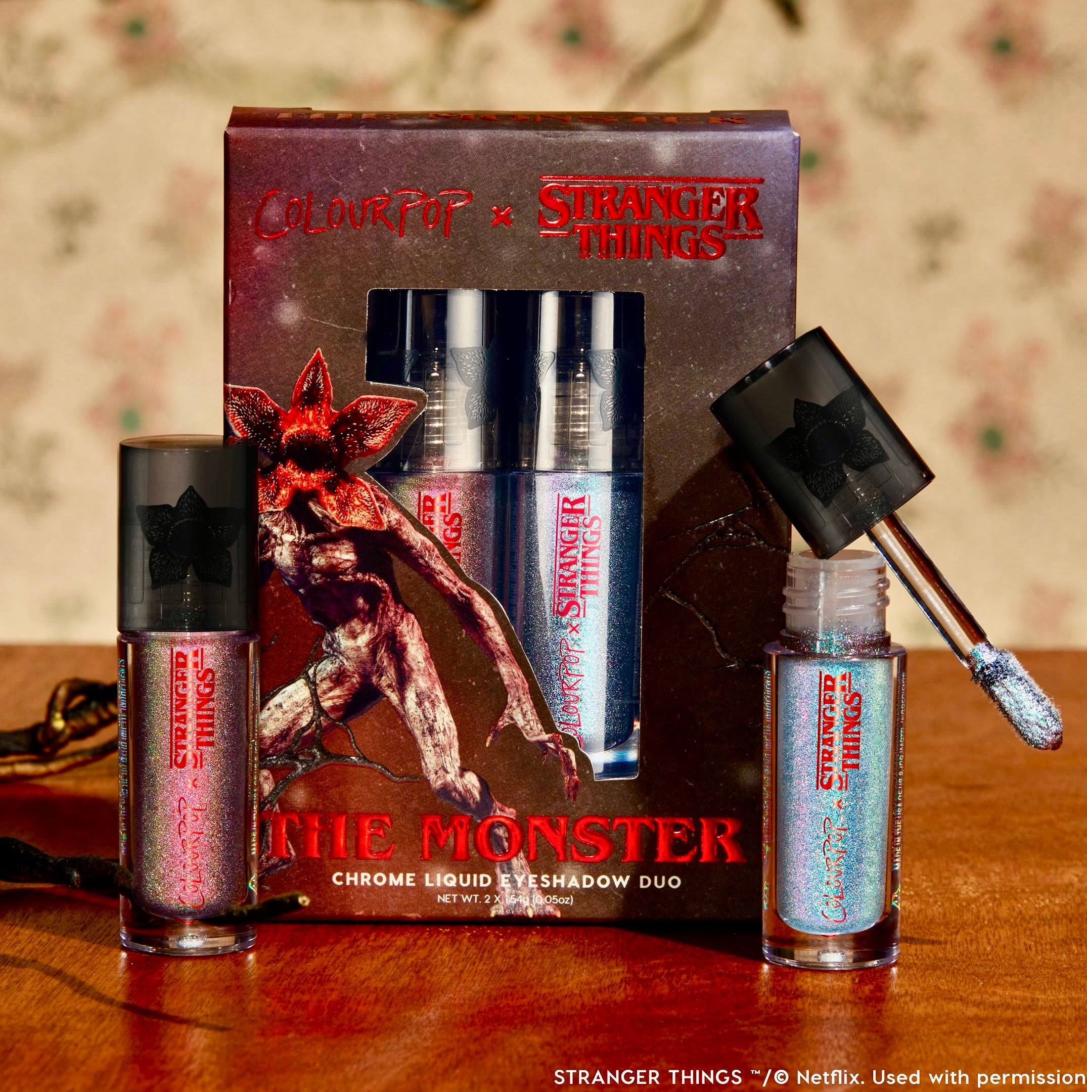 Chrome liquid eyeshadow duo tubes display iridescent blue and pink tones, one wand unscrewed revealing shimmer, in front of “The Monster” box with Demogorgon art - Stranger Things x ColourPop Full Collection ColourPop Chrome Liquid Shadow set.