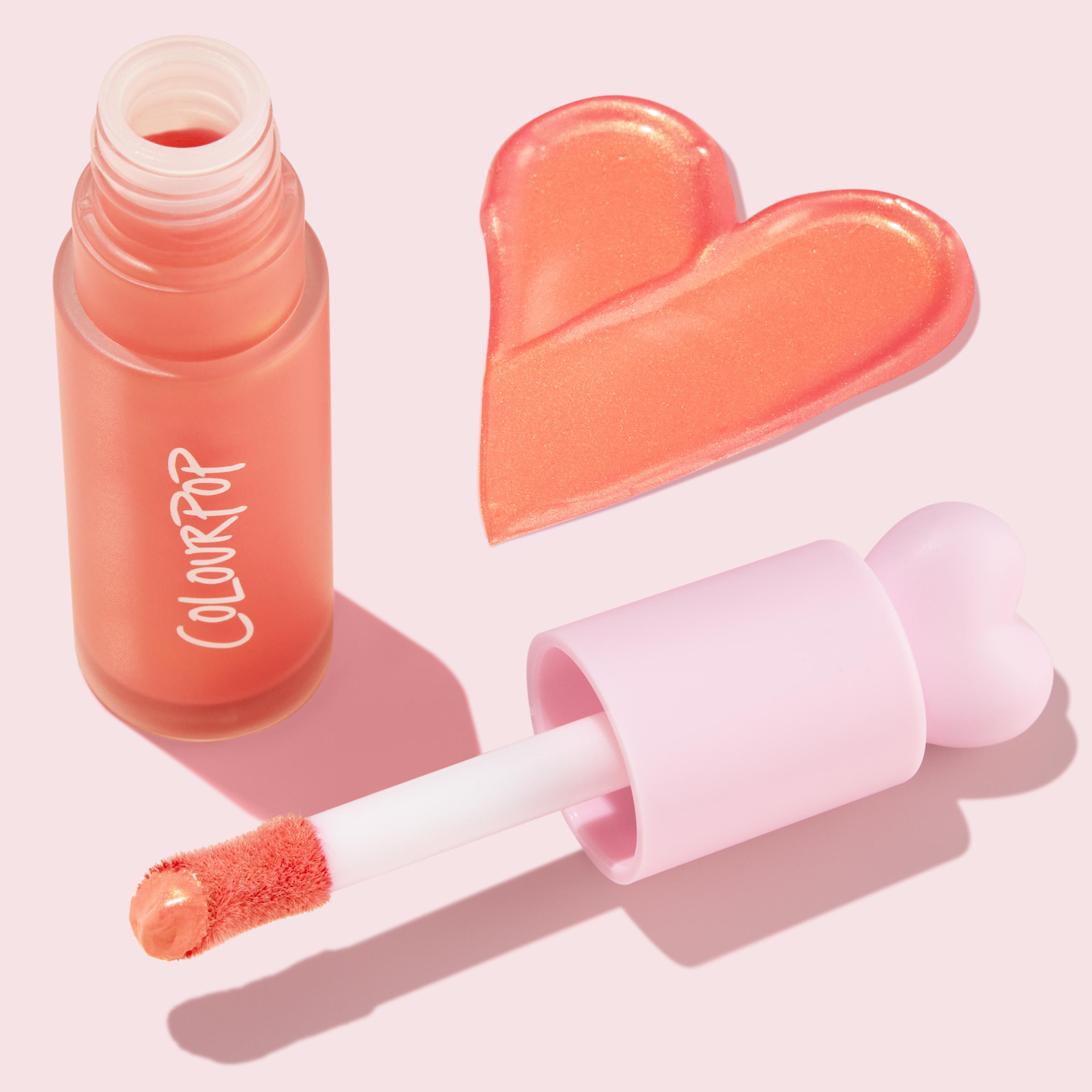 Perfect Peach ColourPop Liquid Blush shown open with doe-foot applicator, frosted peach bottle, and a glossy heart-shaped swatch of peachy shimmer, styled on a pastel pink background with a pink heart cap.