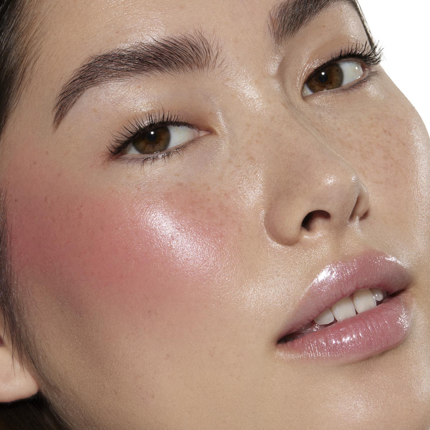 Cheeks glow with dewy rosy pink I Love It by ColourPop Liquid Blush, blending seamlessly to a luminous sheen on a close-up face with natural freckles, brown eyes, and glossy lips, showcasing smooth, buildable color in studio lighting.