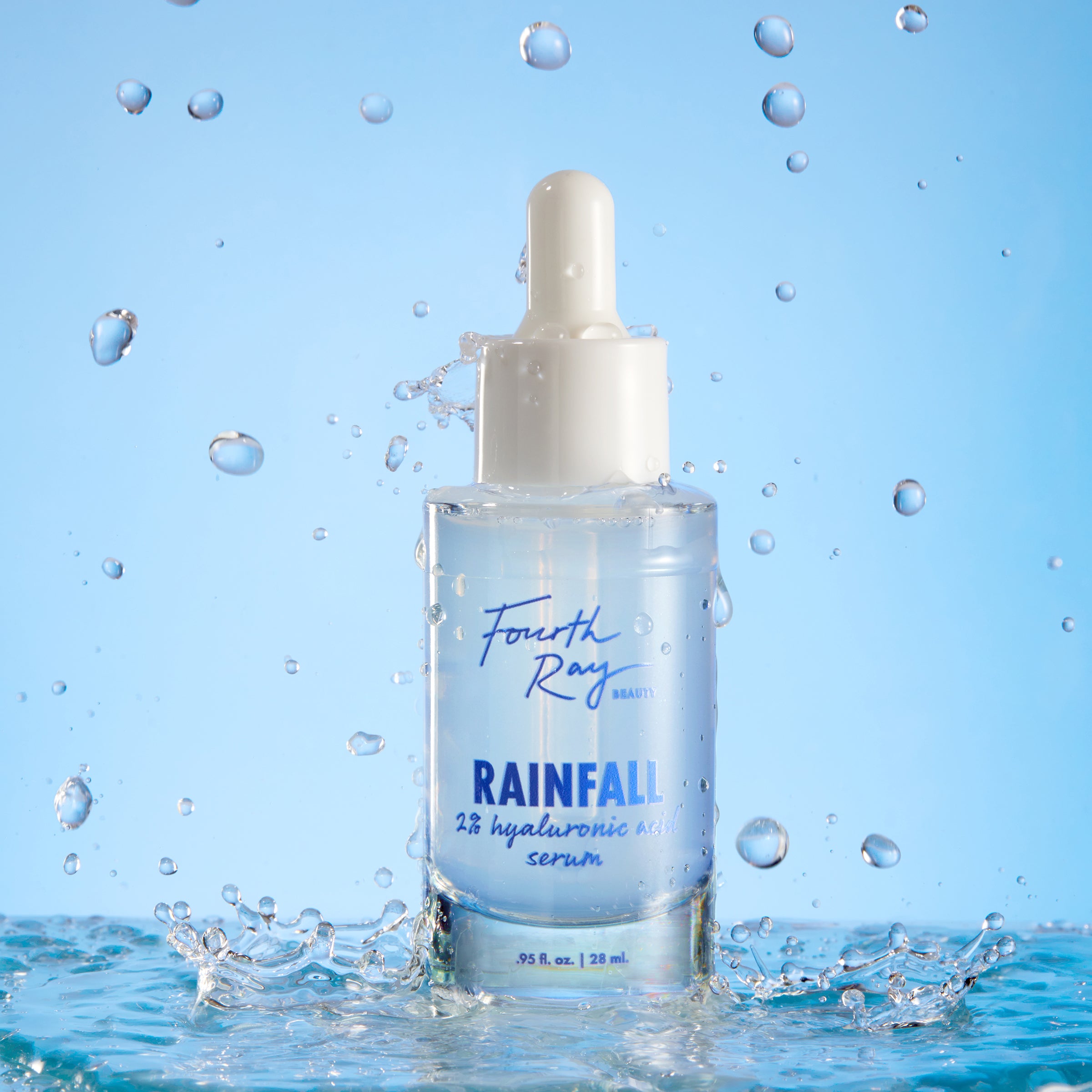Fourth Ray Beauty Rainfall 2% HA Serum dropper bottle standing upright, catching water splashes against a light-blue backdrop, showcasing its hydrating hyaluronic acid formula; ColourPop Face Serum, 0.95 fl oz/28 mL.