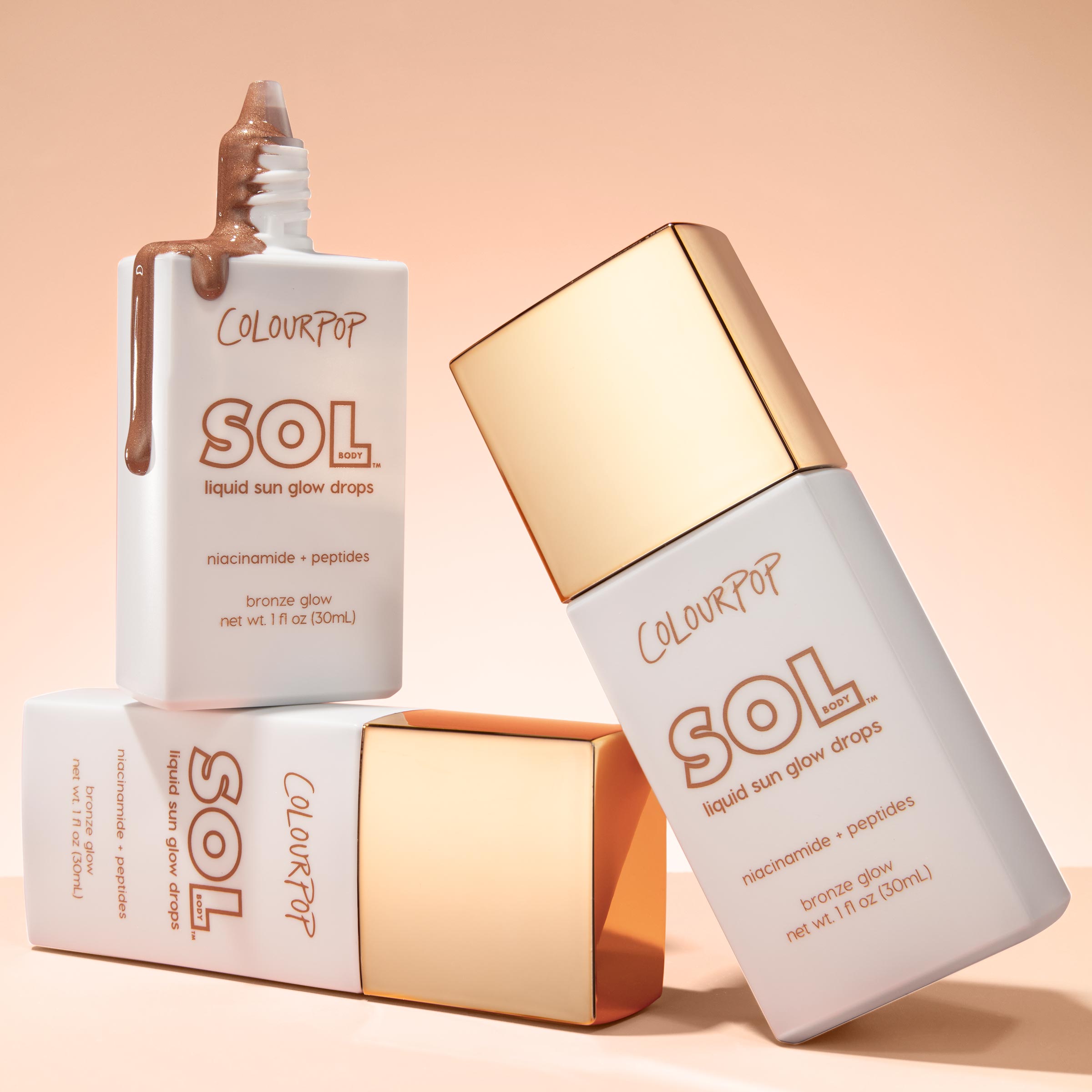 ColourPop SOL Liquid Sun Glow Drops in Bronze Glow drip from an open white bottle while three gold-capped bottles stack on a peach backdrop, highlighting the niacinamide + peptides formula and 1 fl oz (30 mL) size for a radiant bronze glow.
