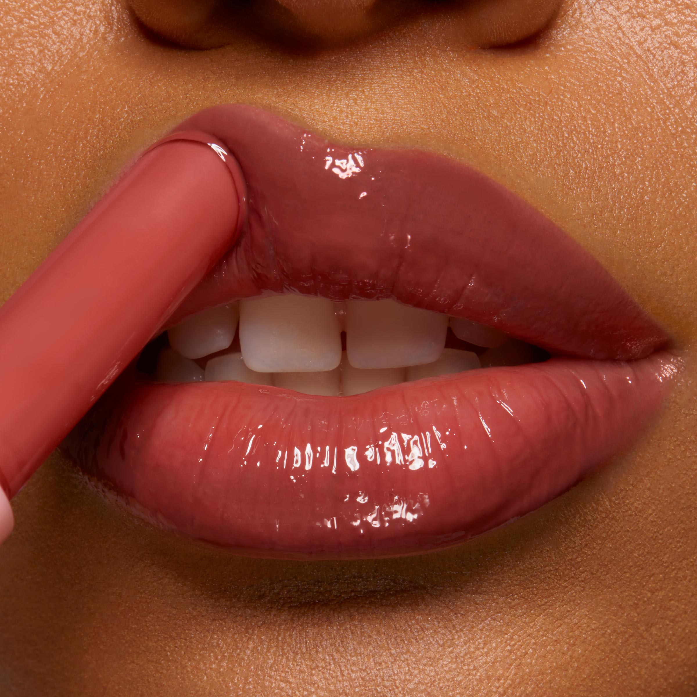ColourPop So Juicy Plumping Gloss Balm with Peptides in PSL glides onto lips from a slim applicator, delivering a high-shine rosy brown finish and plumped look in a tight close-up of a mouth against warm skin.