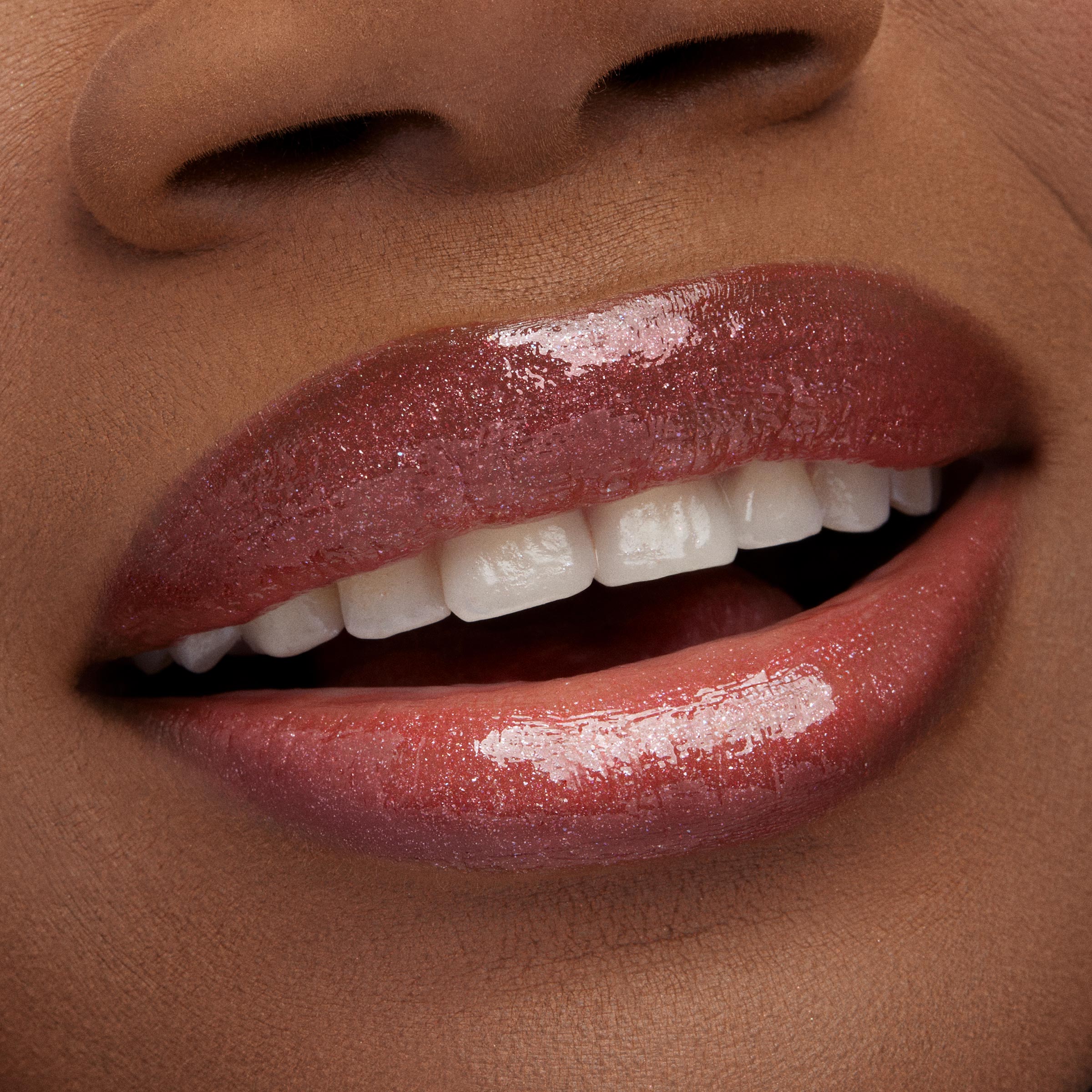 Shimmering lips wear ColourPop Ultra Glossy Lip Yeehaw, a warm rosy-brown gloss with fine sparkle, reflecting light as a slight smile reveals teeth in a macro beauty shot, highlighting the high-shine, smooth finish.