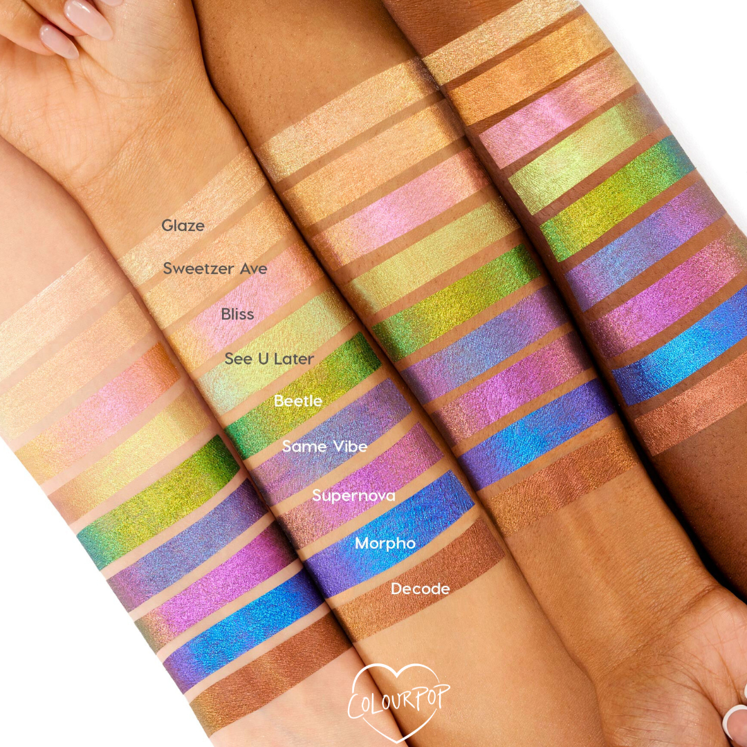 Feelin’ Bold ColourPop Chrome Liquid Shadow swatches gleam on four forearms, showing multi‑chrome shifts from gold, pink, lime, and teal to blue and copper; shade names like Glaze, Beetle, Morpho, and Decode appear beside each stripe for comparison.