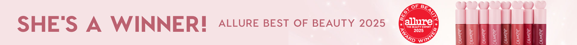 ColourPop lip tints lined up in pink tubes with heart-shaped caps, showcasing nude to deep berry shades, positioned beside an Allure Best of Beauty 2025 winner badge with the headline She's a winner! on a soft pink banner.