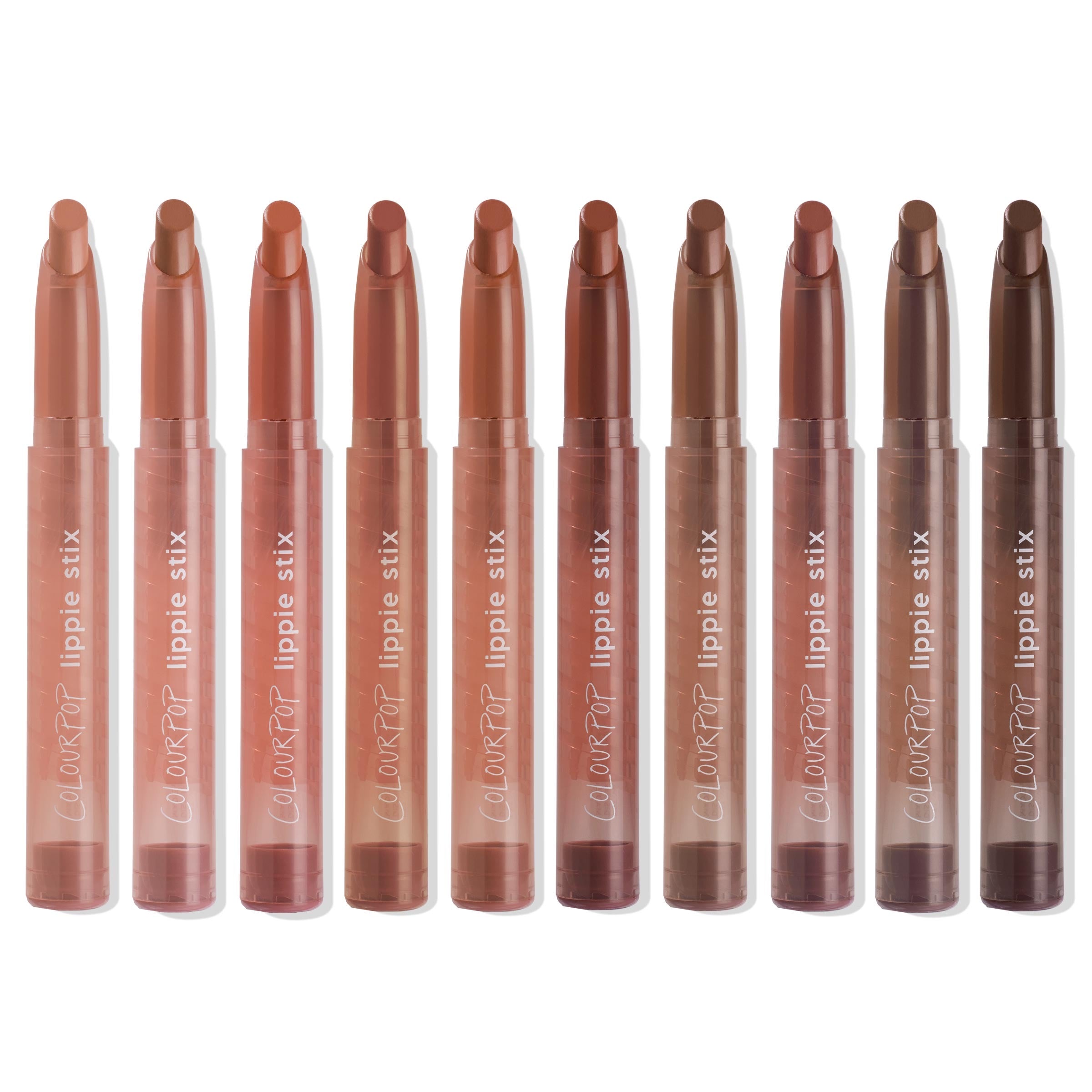 ColourPop Lippie Stix line up showing In the Nude collection - ten twist-up lipsticks in clear tubes, ranging from peach and pinky beige to warm caramel and deep brown - standing upright on a white background.
