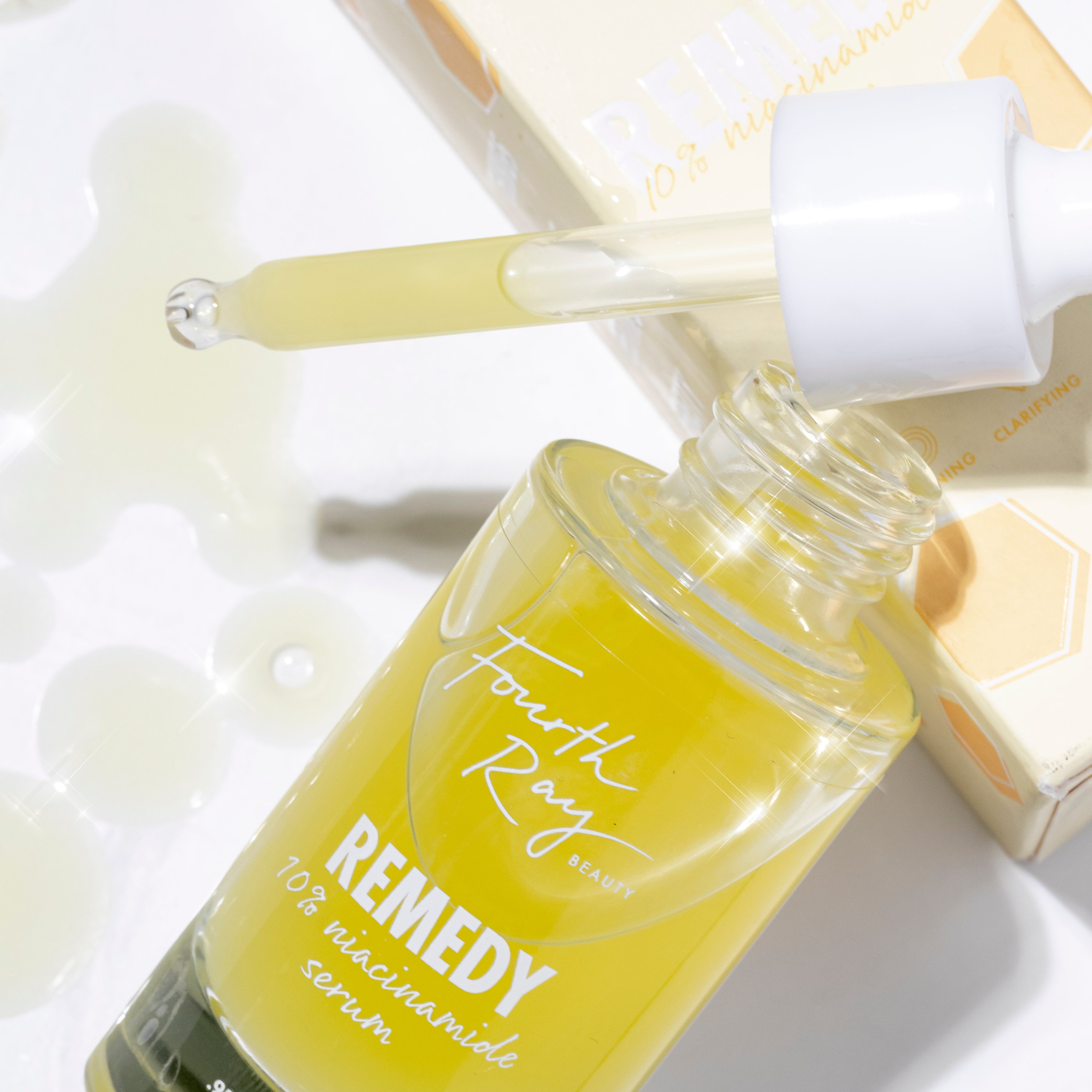 Fourth Ray Beauty Remedy 10% niacinamide serum bottle with white dropper dispensing pale yellow formula, set beside its cream box on a white surface with serum splashes; So Refined ColourPop Face Set skincare.