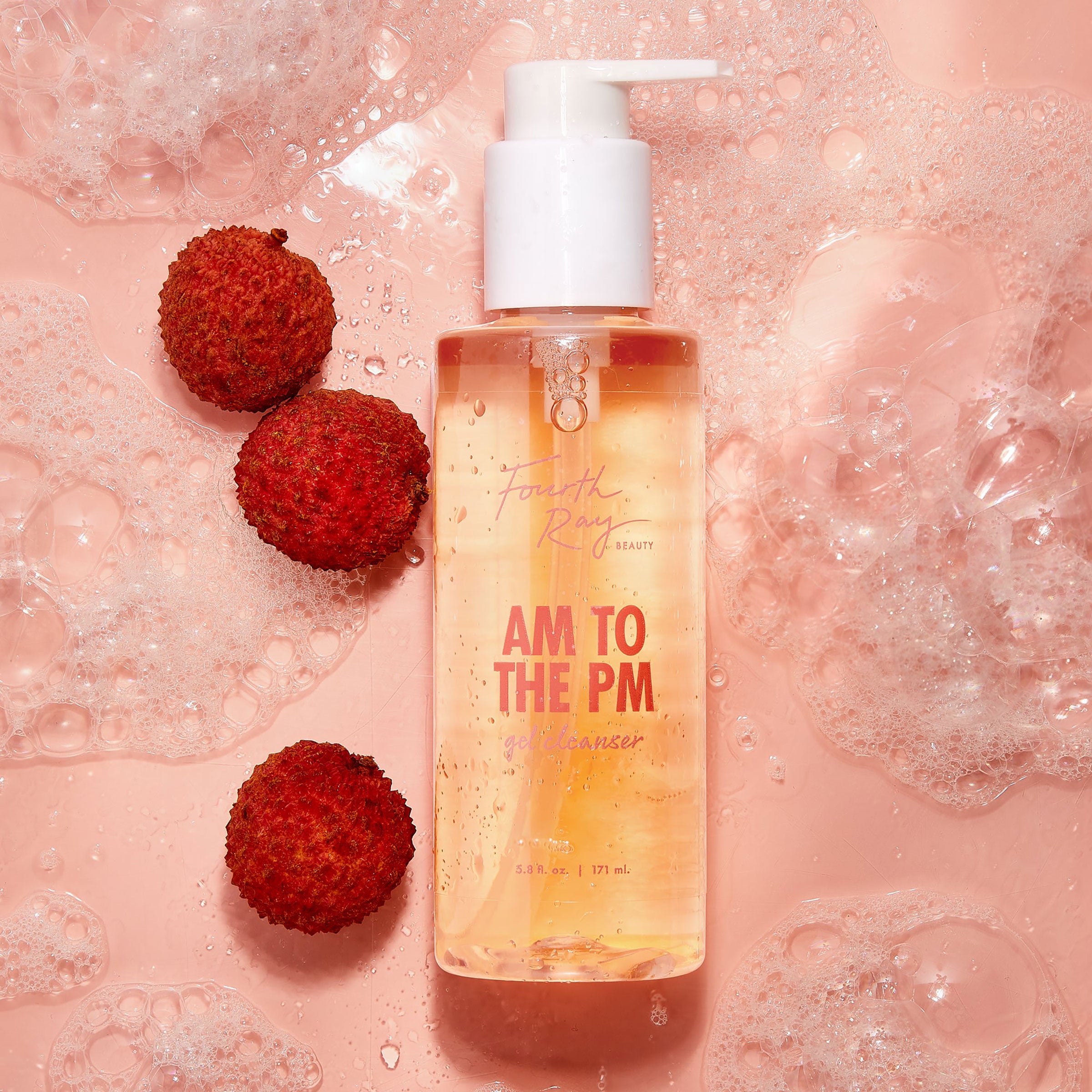 Clear pump bottle of Fourth Ray Beauty AM to the PM Gel Cleanser by ColourPop glistening with golden gel, sitting amid foamy suds on a pink surface next to lychees; 5.8 fl oz face cleanser.