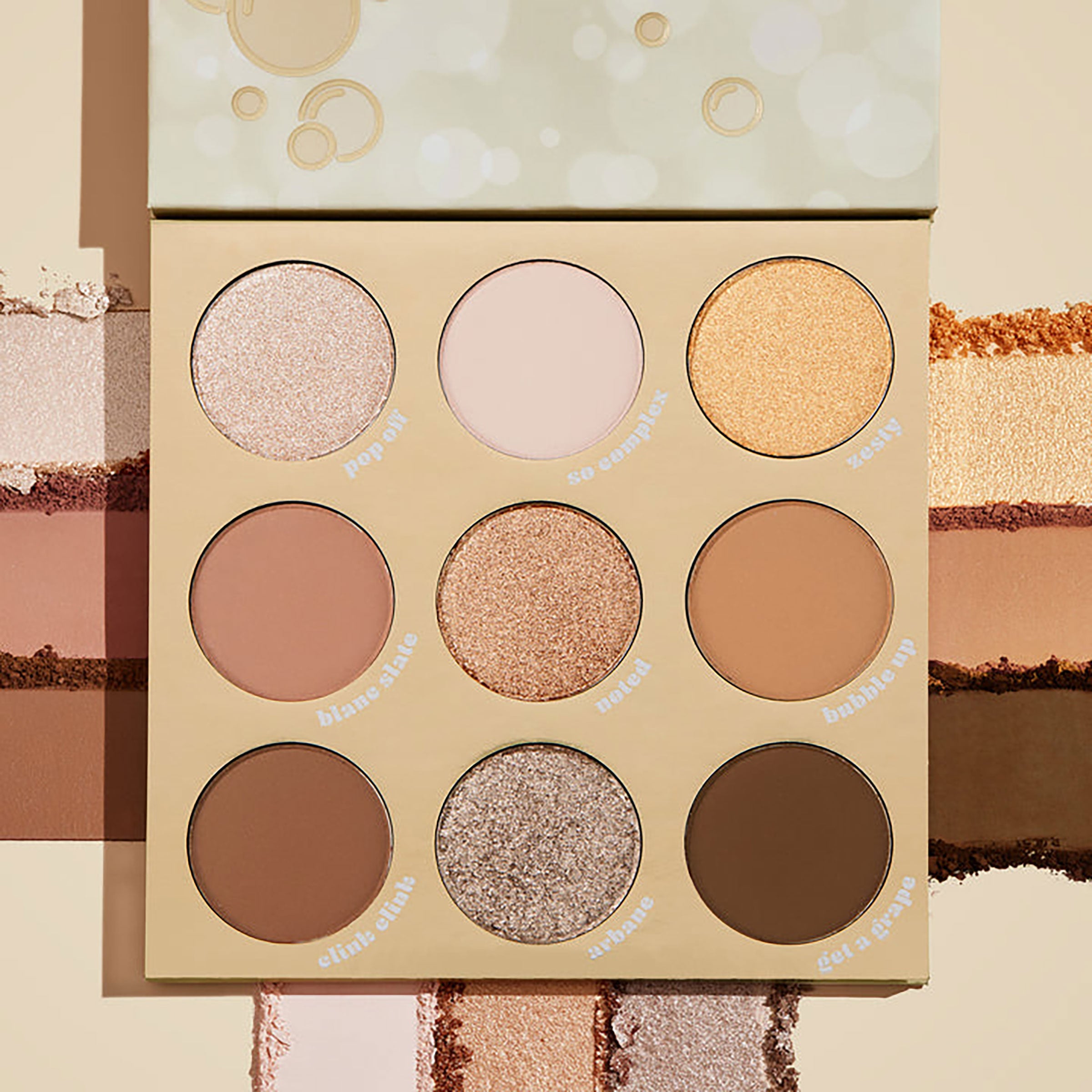 ColourPop Feelin' Bubbly shadow palette open, showing a 9-pan range of champagne, gold, taupe, and brown shades in matte and shimmer finishes, set on a cream backdrop with pigment swatches and bubbly-themed beige packaging.